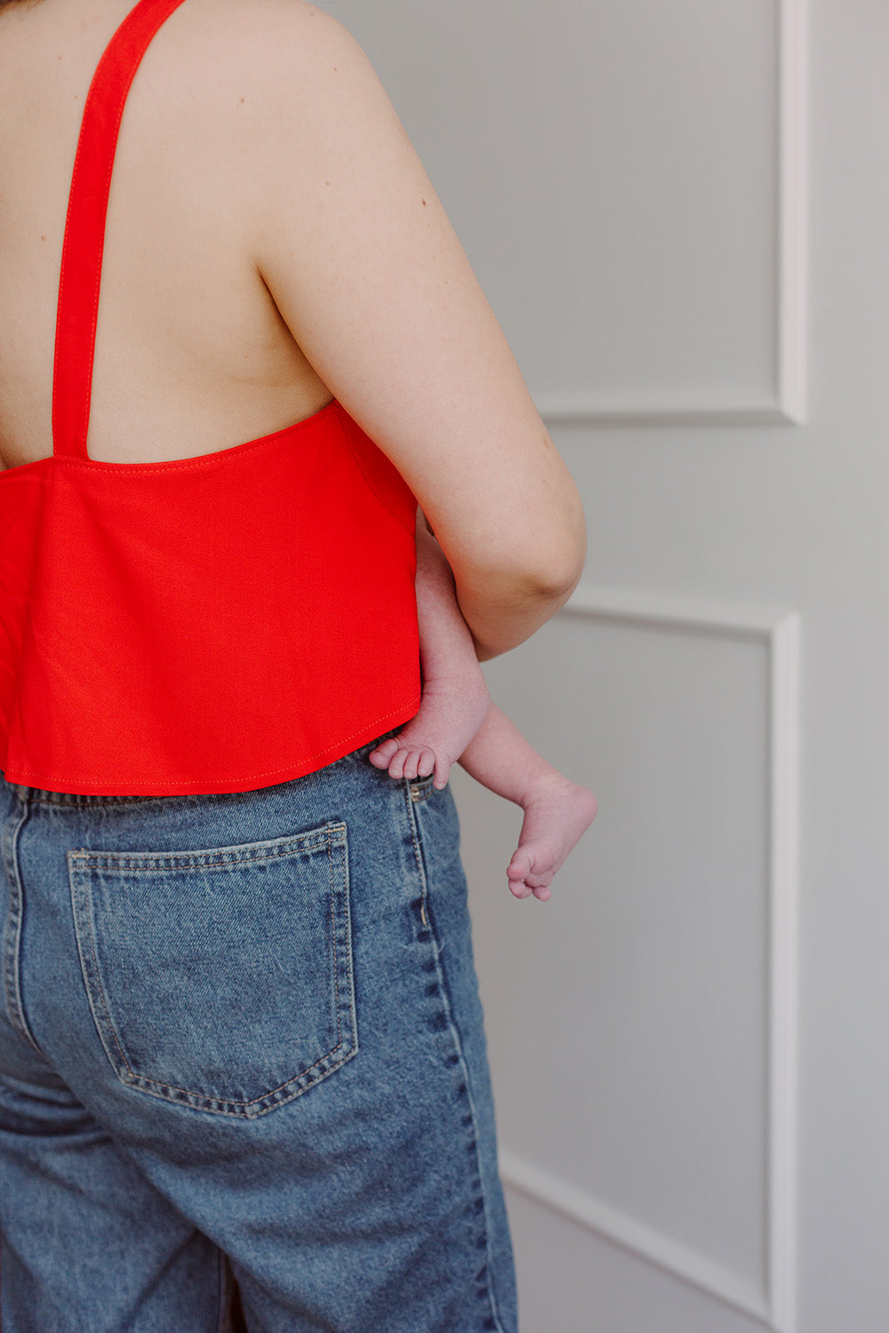 Mujer de espaldas cargando un bebe usando una blusa color rojo.