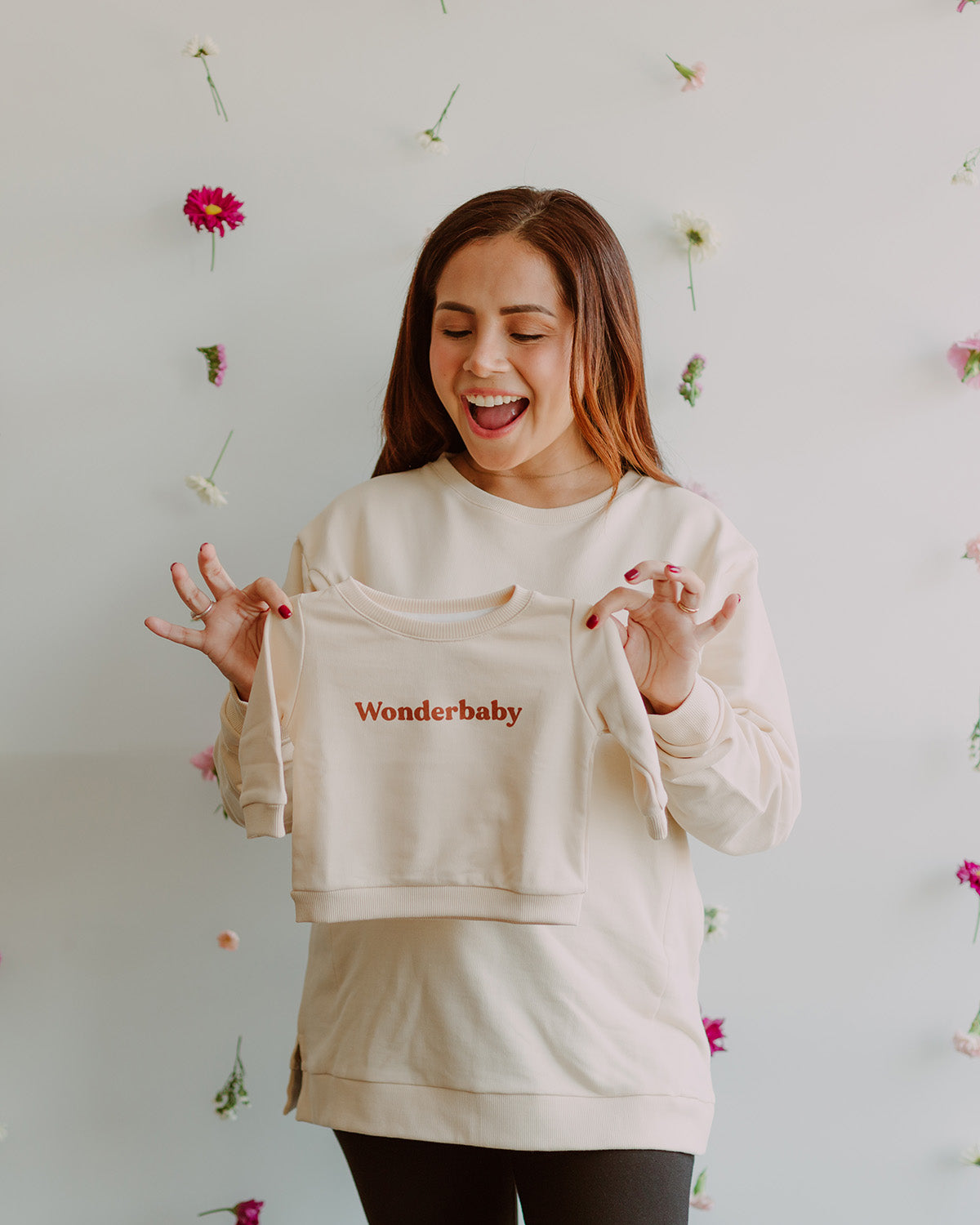 Mujer embarazada usando un polo color vainilla. En sus manos sostiene un polo de talla de bebe igual al que lleva puesto.