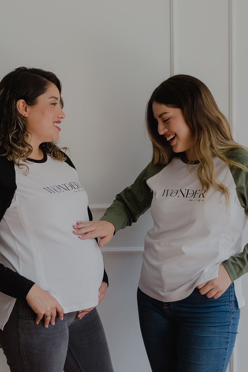 Dos mujeres usando un polo manga larga de color verde y blanco. Una de ellas está embarazada.