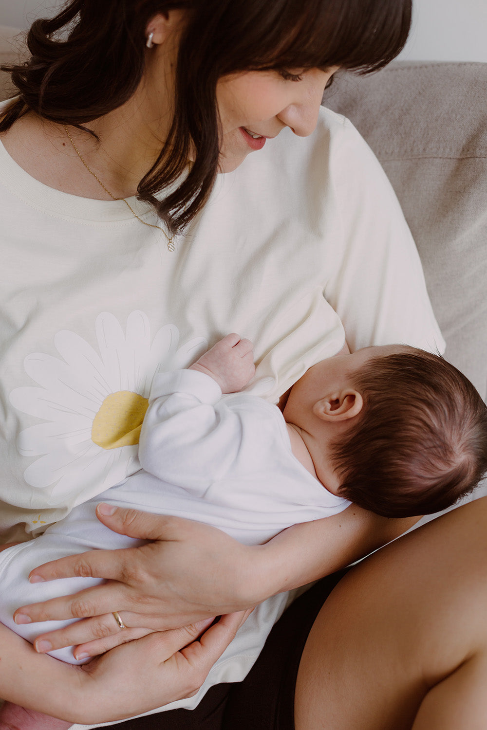 Mujer usando un polo blanco. En sus brazos carga a un bebe al que le está dando de lactar.