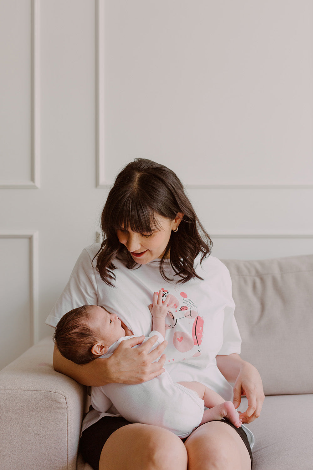 Mujer usando un polo color blanco. En sus brazos sostiene a un bebe al que le está dando de lactar.