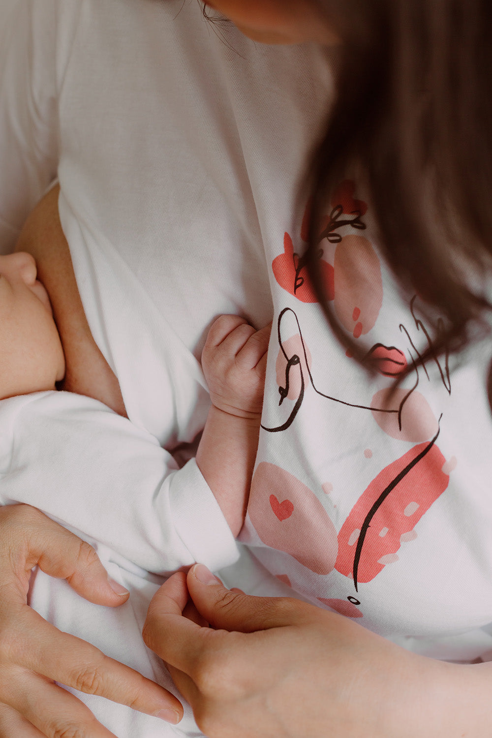 Mujer usando un polo color blanco. En sus brazos sostiene a un bebe al que le está dando de lactar.