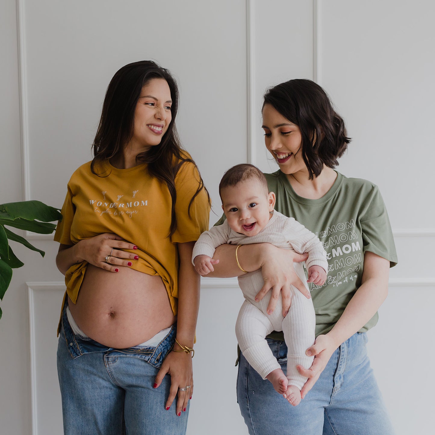 Dos mujeres sonriendo. La de la izquierda está embaraza y utiliza un polo color albaricoque. La mujer de la derecha usa un polo verde y carga a un bebe.