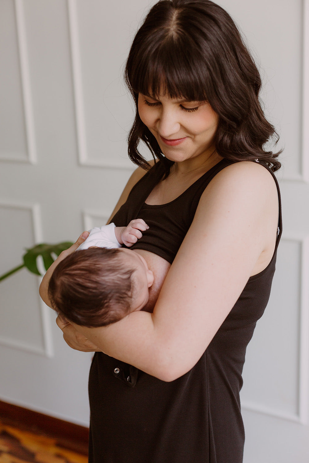 Mujer usando un vestido negro. En sus brazos sostiene a un bebe al cual le da de lactar.