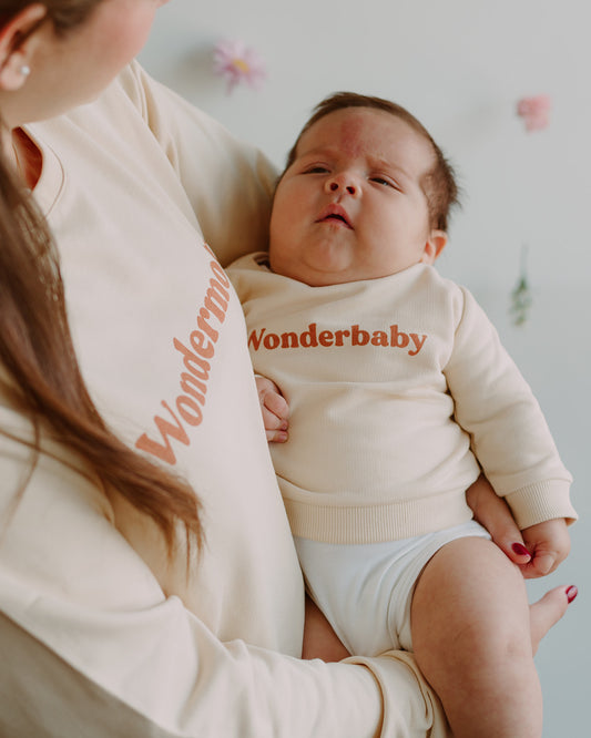 Mujer cargando a un bebe. Ambos llevan un polo manga larga color vainilla.