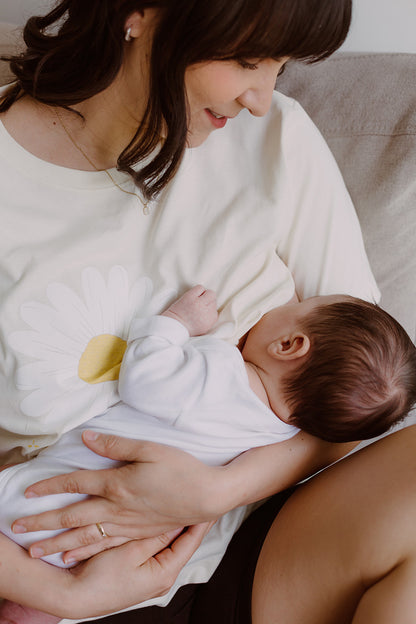 Mujer usando un polo blanco. En sus brazos carga a un bebe al que le está dando de lactar. 