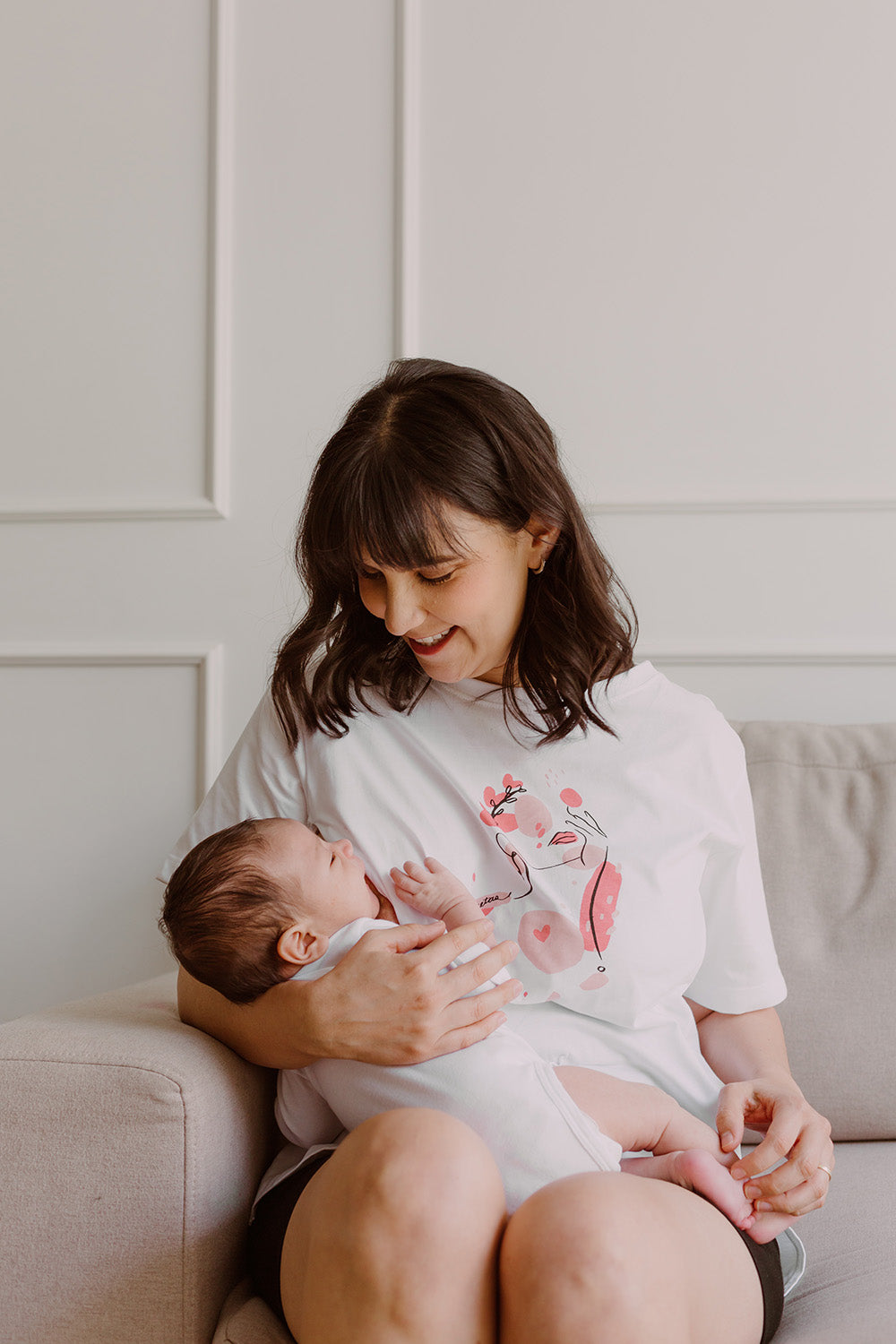 Mujer usando un polo color blanco. En sus brazos sostiene a un bebe al que le está dando de lactar. 