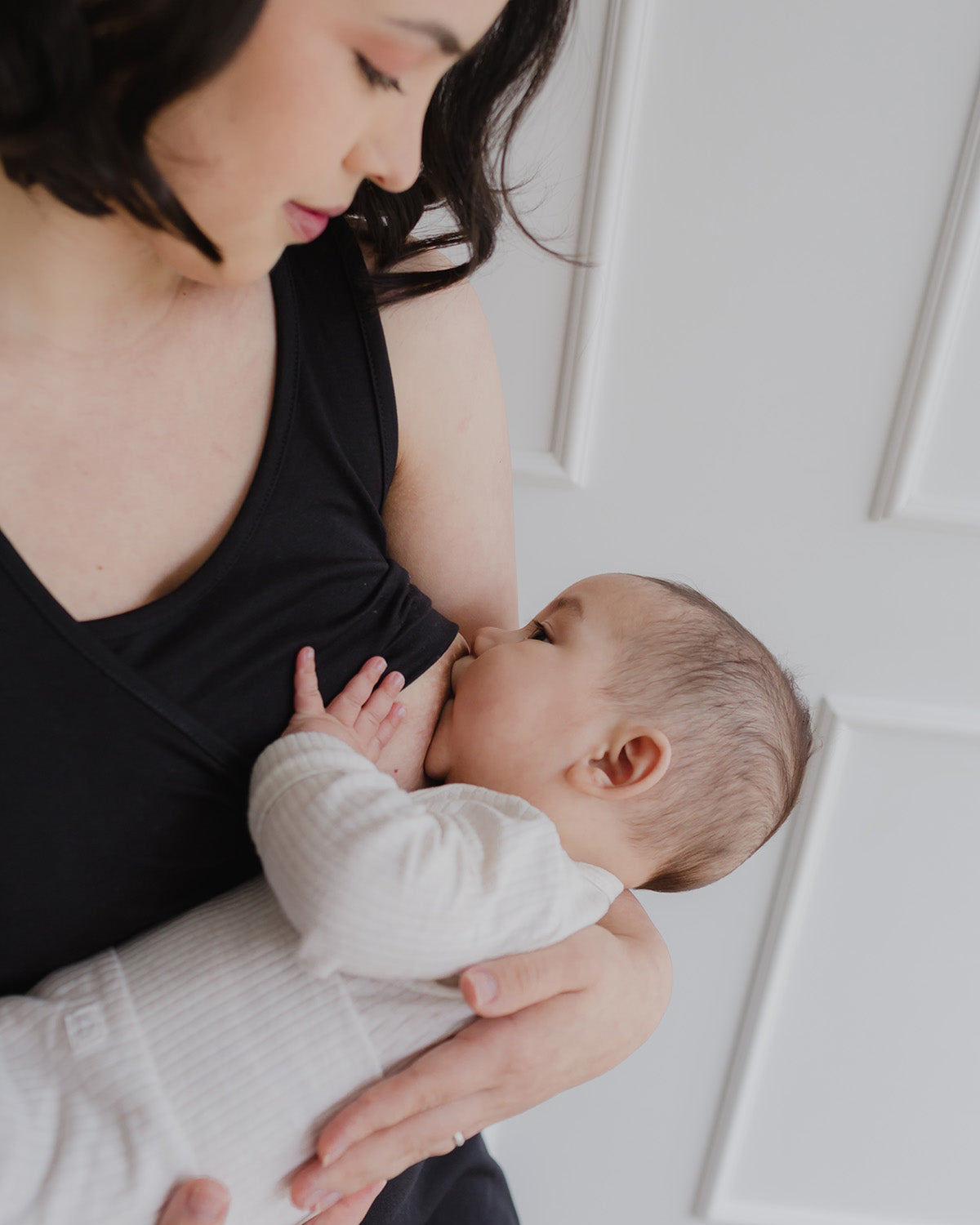 Mujer usando un vestido negro. En sus brazos sostiene a un bebe al cual le da de lactar.