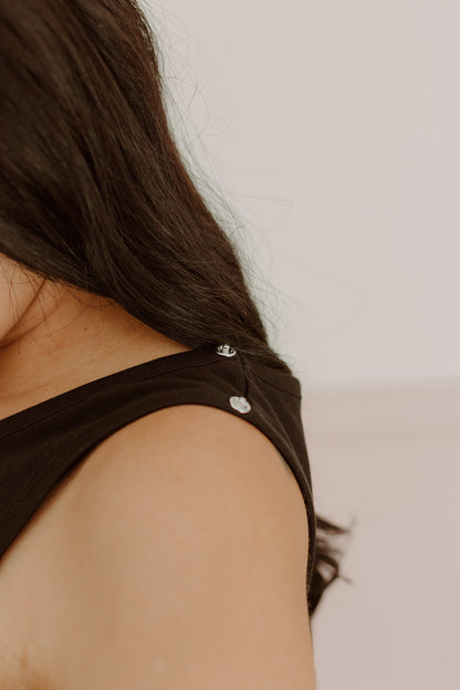 Acercamiento de los broches en la tira de un vestido negro a la altura del hombro.
